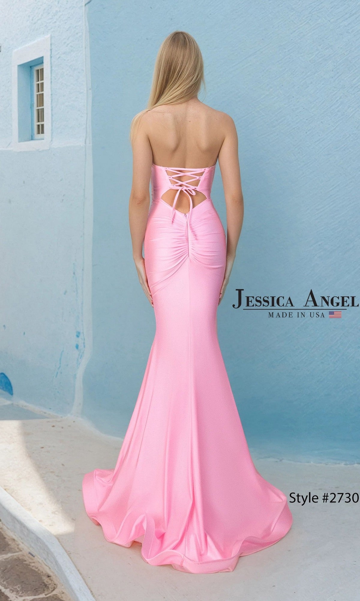 A woman stands on a blue and white street, her back to the camera, wearing the Jessica Angel 2730 long prom dress—a strapless pink satin-jersey gown with lace-up back detailing.